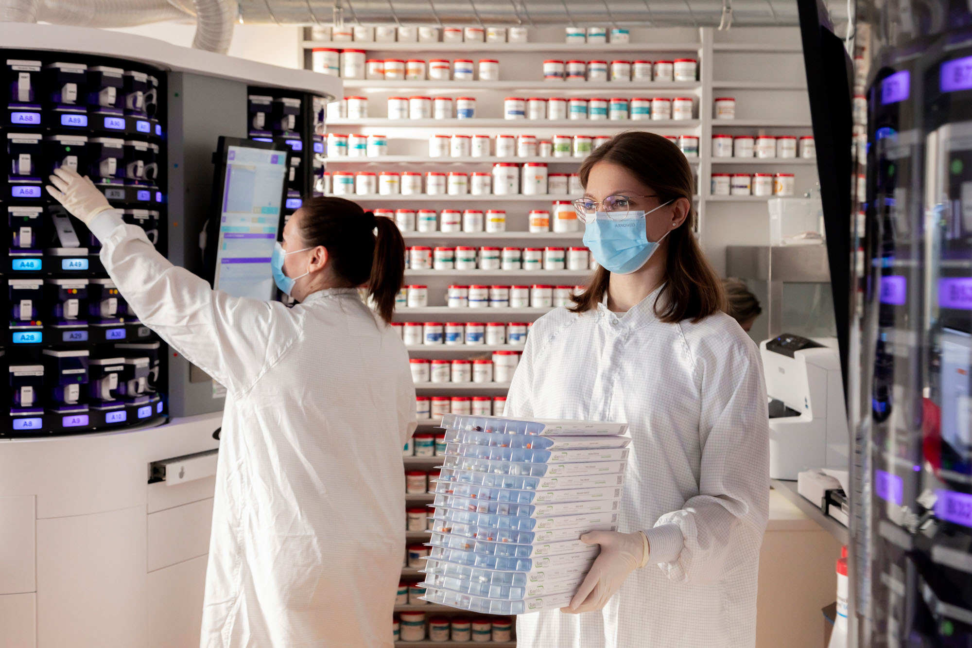 Neue Apotheke_Anja Grothe Fotografie_Arbeit_069 Zwei Mitarbeiterinnen im Blisterzentrum: eine am Blisterautomaten und eine trägt einen Stapel Blisterkarten